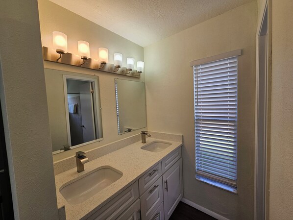 A bathroom with two sinks, a large mirror, and a window with blinds.