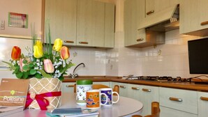 A kitchen with light-colored cabinets, a round table with a bouquet of flowers, and a coffee maker. - Seaside Apartment in Rosolina Mare (Rosolina)