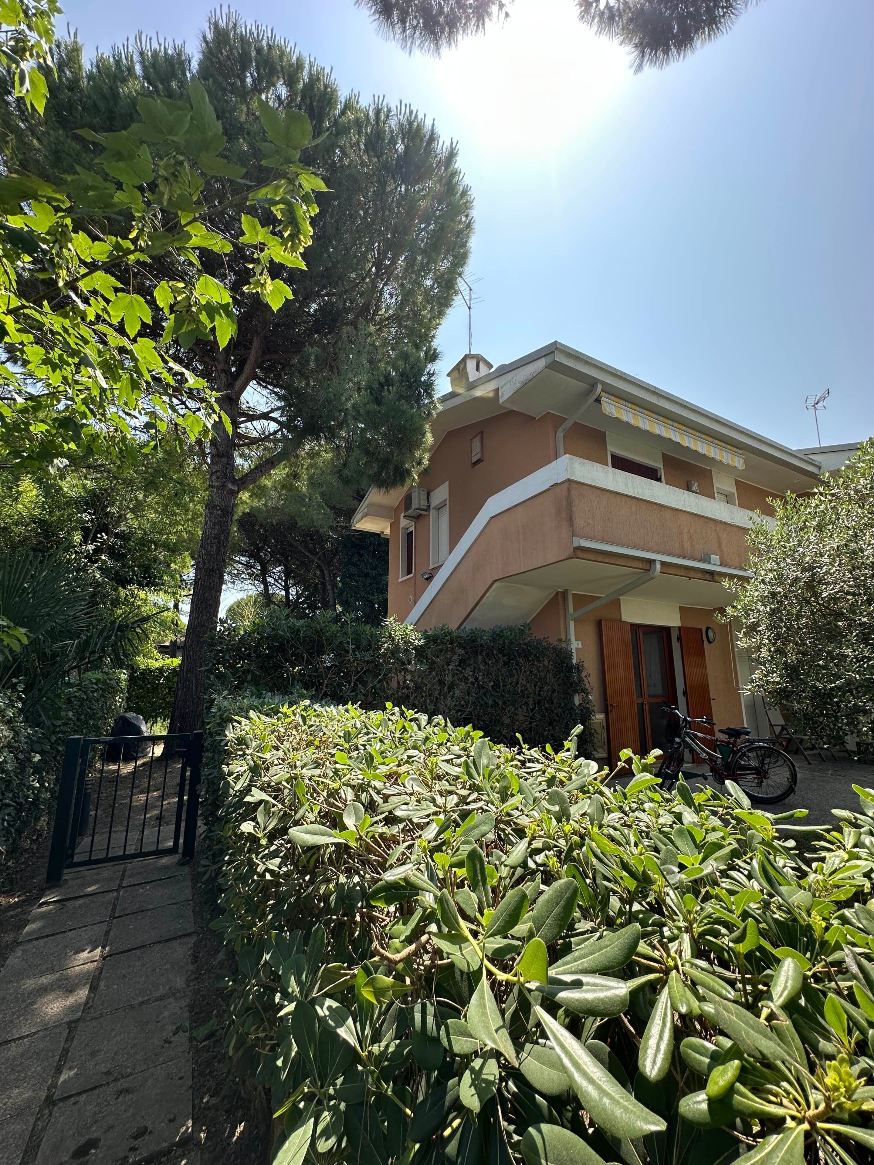 A two-story building with a balcony, surrounded by greenery and a gate.