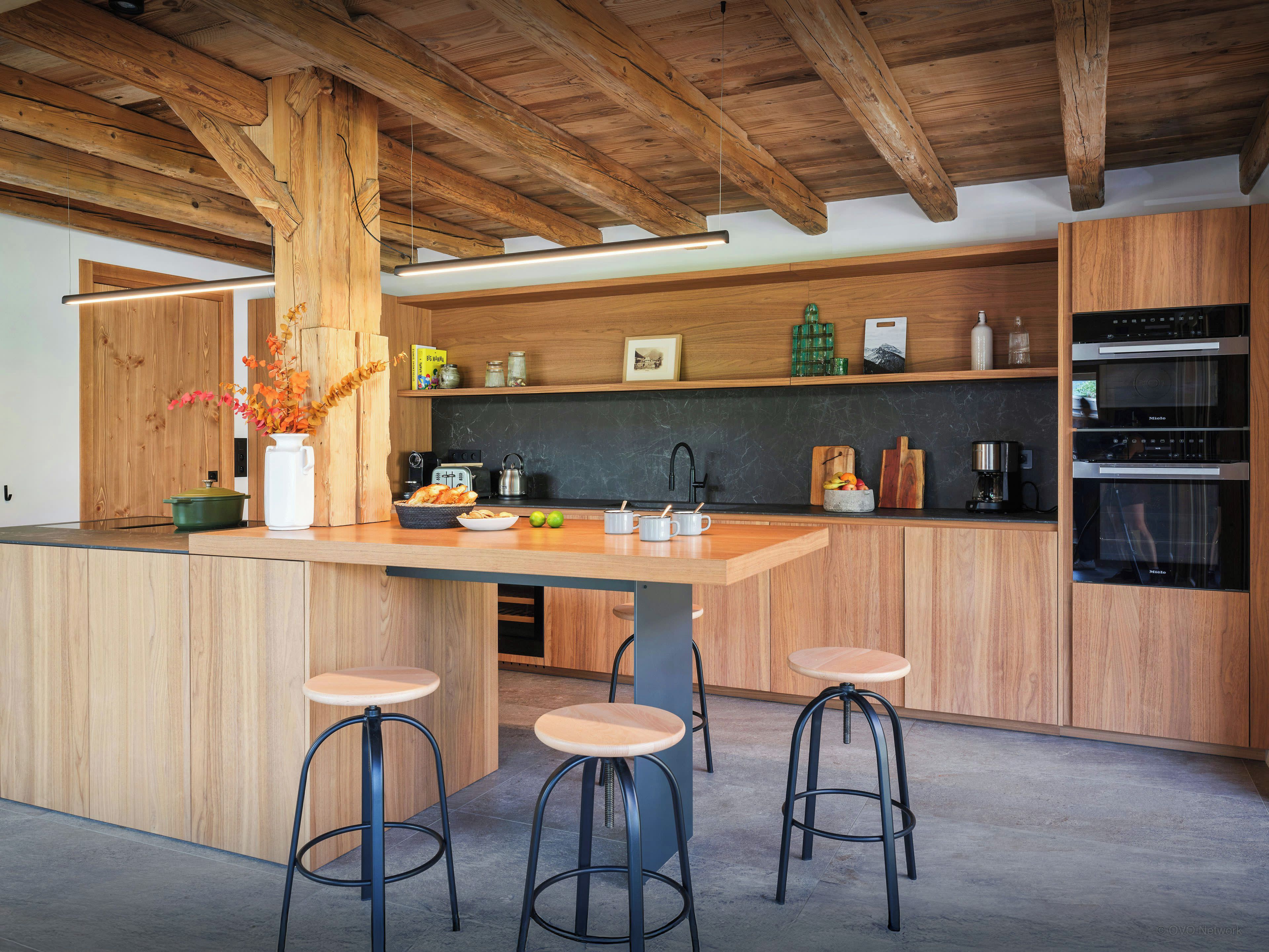 A modern kitchen with wooden cabinetry, a central island with stools, and built-in appliances.