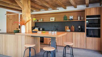 A modern kitchen with wooden cabinetry, a central island with stools, and built-in appliances.