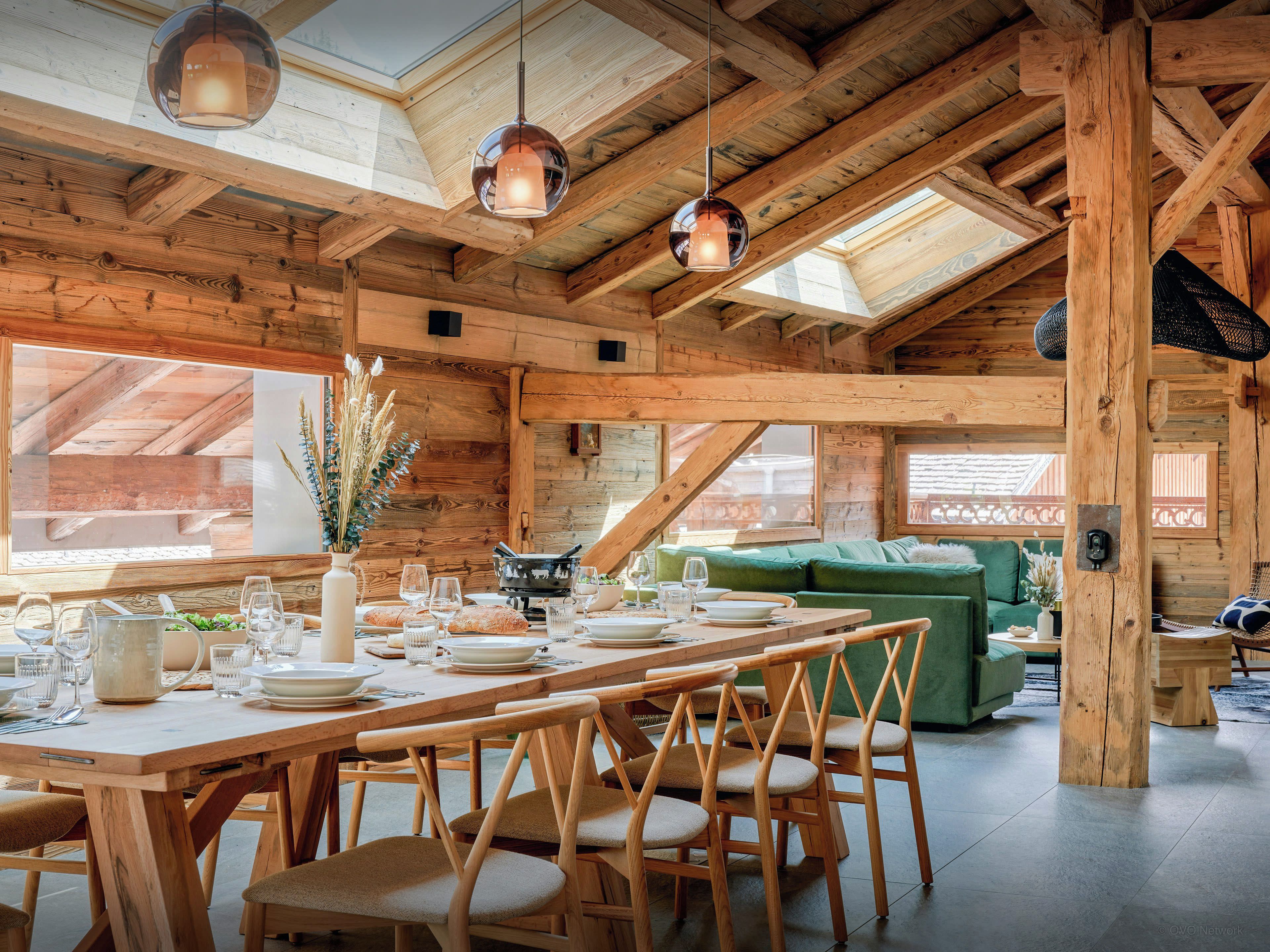 Un intérieur en bois comprenant un coin repas, des chaises en bois, une table dressée pour un repas et un canapé vert.