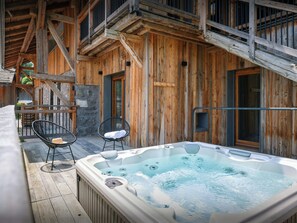 Una cabaña de madera con un jacuzzi, dos sillas y una escalera.