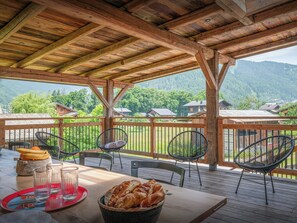 Una terrassa de fusta amb taula preparada per dinar, cadires i vista a un paisatge de muntanyes.