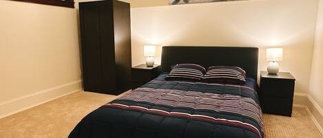 Ein Schlafzimmer mit einem dunkelbraunen Bett, zwei Nachttischlampen, einem dunklen Kleiderschrank und einem Blumenbild an der Wand.