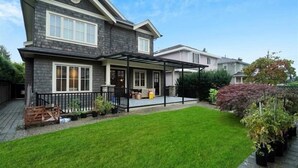 A two-story house with a covered patio, a well-maintained lawn, and a variety of potted plants.