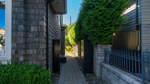 A narrow pathway between two buildings with a stone wall on one side and a metal fence on the other.