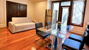 A modern living room with a glass dining table, a sofa, and a refrigerator.