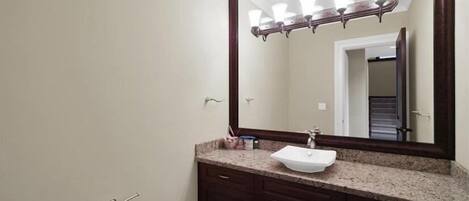 Un baño con un espejo grande, un lavabo y armarios de madera oscura.