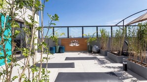 A rooftop patio with exercise mats, potted plants, and a wooden wall with a decorative element. - Spin Stays (São Paulo)