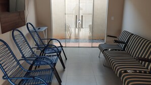 A room with a sofa, two blue chairs, a small table, and a TV mounted on the wall.