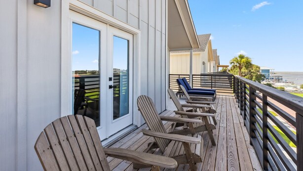 A wooden deck with Adirondack chairs and a glass door leading to a room.