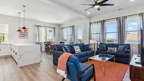 A spacious living area with a blue sofa, a coffee table, and a modern ceiling fan.