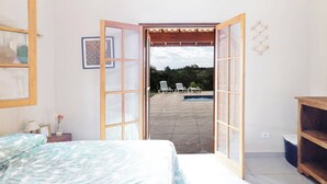 A bedroom with a bed, a wooden shelf, and a view of an outdoor patio with chairs and a pool. - Ch Cara com Piscina Churrasq e Wifi pet Friendly (Ibiuna)