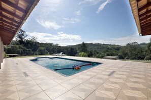A swimming pool with a hot tub and lounge chairs, surrounded by a tiled patio and a view of a hilly landscape.