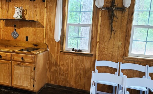 Una habitación rústica de madera con un armario de madera, una ventana con vista a árboles y sillas blancas.