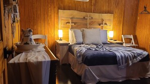 Une chambre chaleureuse avec une tête de lit en bois, deux tables de chevet avec des lampes, un lit recouvert d’une couverture à rayures et une petite table ornée d’un objet décoratif.