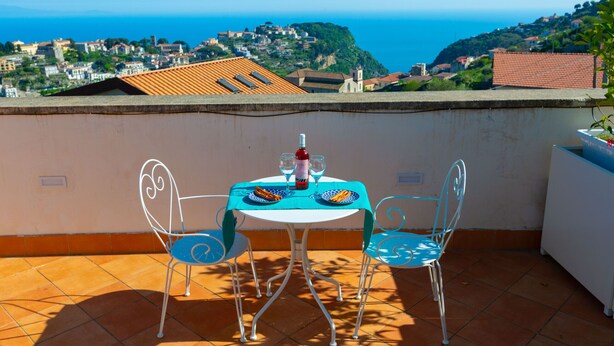 A terrace with a table and chairs, overlooking a coastal town with buildings and a view of the sea. - De Pando - Campidoglio (Scala)