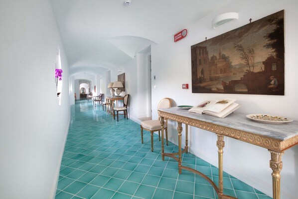 A hotel corridor with a blue-tiled floor, a dining table with chairs, and a large painting on the wall. - De Pando - Campidoglio (Scala)