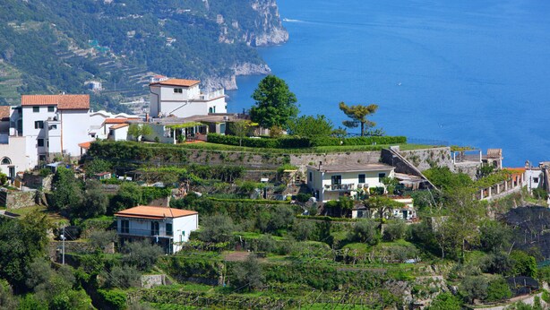 A coastal village with terraced houses, a clear view of the sea, and a mountainous backdrop.