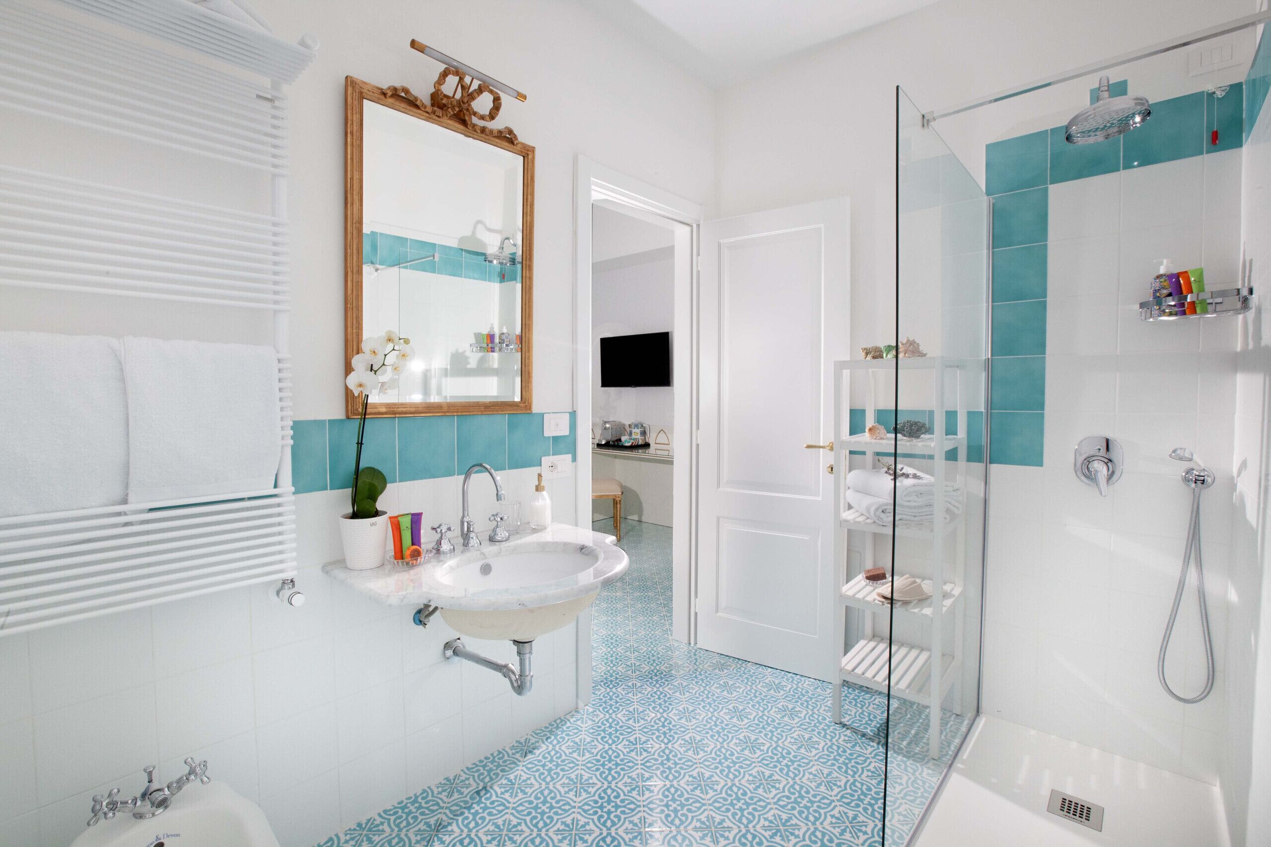 Uma casa de banho moderna com lavatório branco, cabine de duche em vidro e chão com padrão azul.