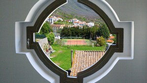 A view through a window with a decorative frame, revealing a tennis court, a green area, and buildings in the background.