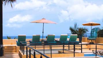 A poolside area with lounge chairs and umbrellas, overlooking the ocean.