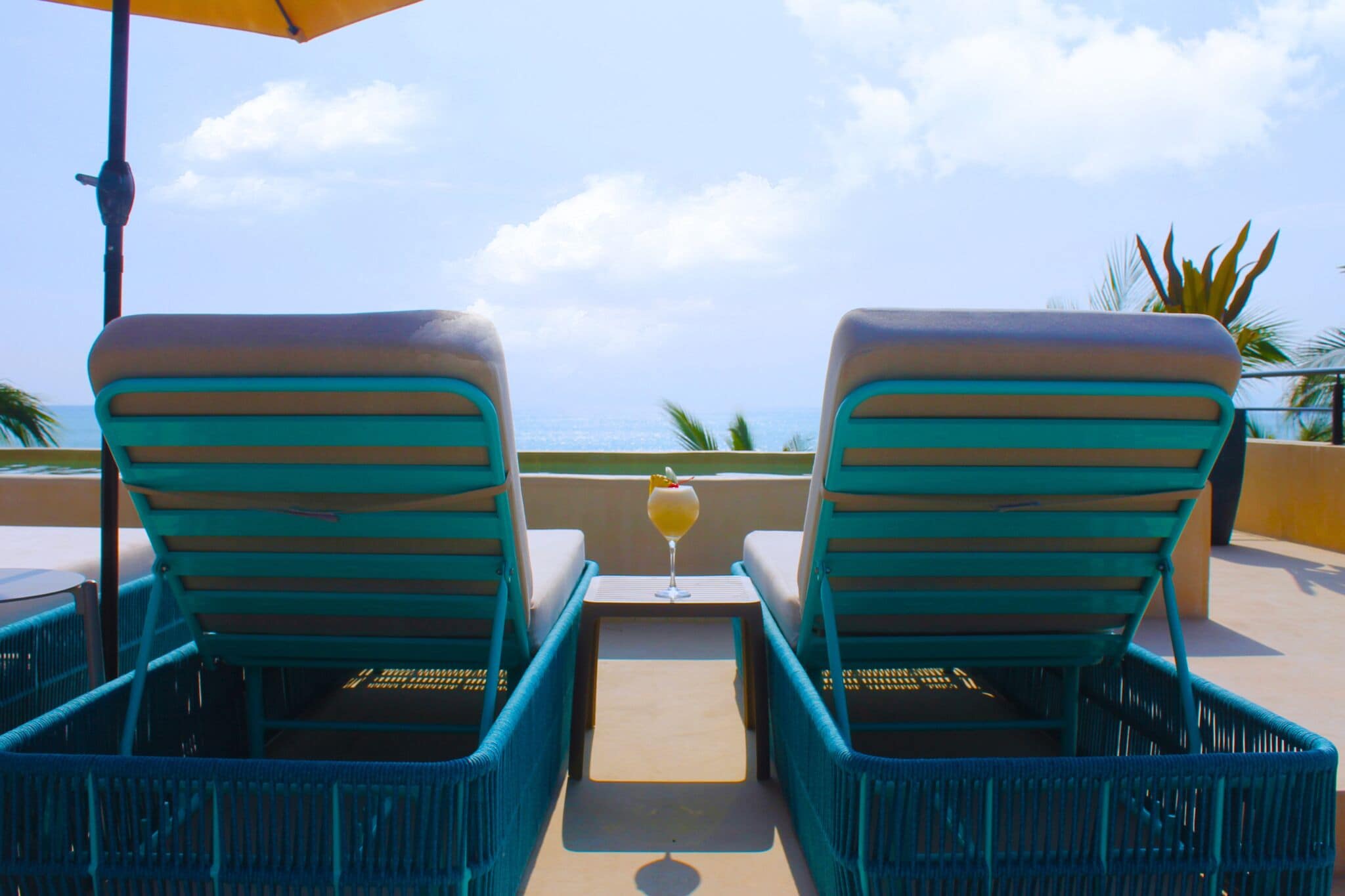 Dos sillones de relax mirando a una piscina, con un vaso de bebida sobre una mesita entre ellos.