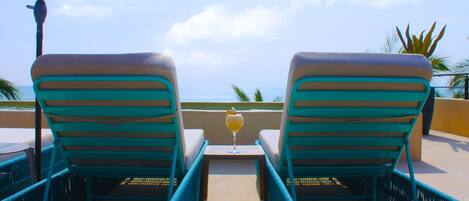 Dos sillones de relax mirando a una piscina, con un vaso de bebida sobre una mesita entre ellos.