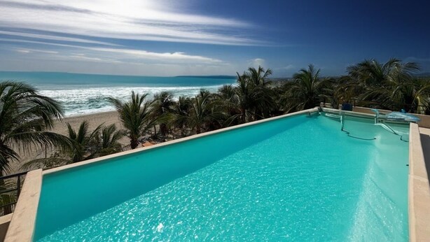 Piscina azul translúcida com vista para o oceano e palmeiras.