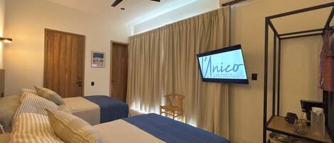 A hotel room with two beds, a ceiling fan, a TV displaying 'Unico', and a wooden door.