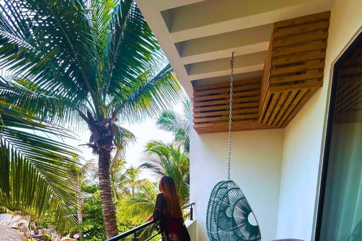 Un balcón con vista a palmeras, una silla colgante y una pequeña mesa.