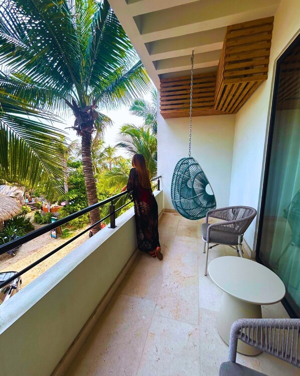 A balcony with a view of palm trees, a hanging chair, and a small table.