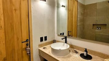 A bathroom with a wooden door, a large mirror, a white sink, and a towel rack.