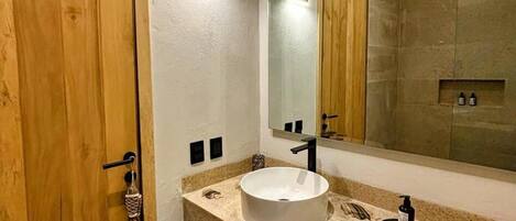 Une salle de bain avec une porte en bois, un grand miroir, un lavabo blanc et un porte-serviettes.