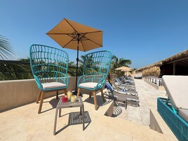 Una terraza en la azotea con sillas de mimbre turquesa, una mesa con bebidas y sillones de relax.