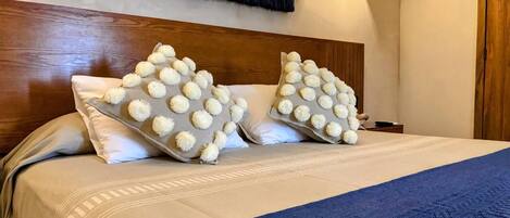 Una cama bien hecha con un edredón azul y dos almohadas adornadas con pompones blancos.
