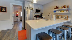 Een moderne keuken met roestvrijstalen apparatuur, een wit kookeiland met barkrukken en een magnetron boven de kasten.