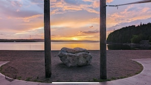 Vista del atardecer con una roca grande al frente y una estructura de madera al fondo.