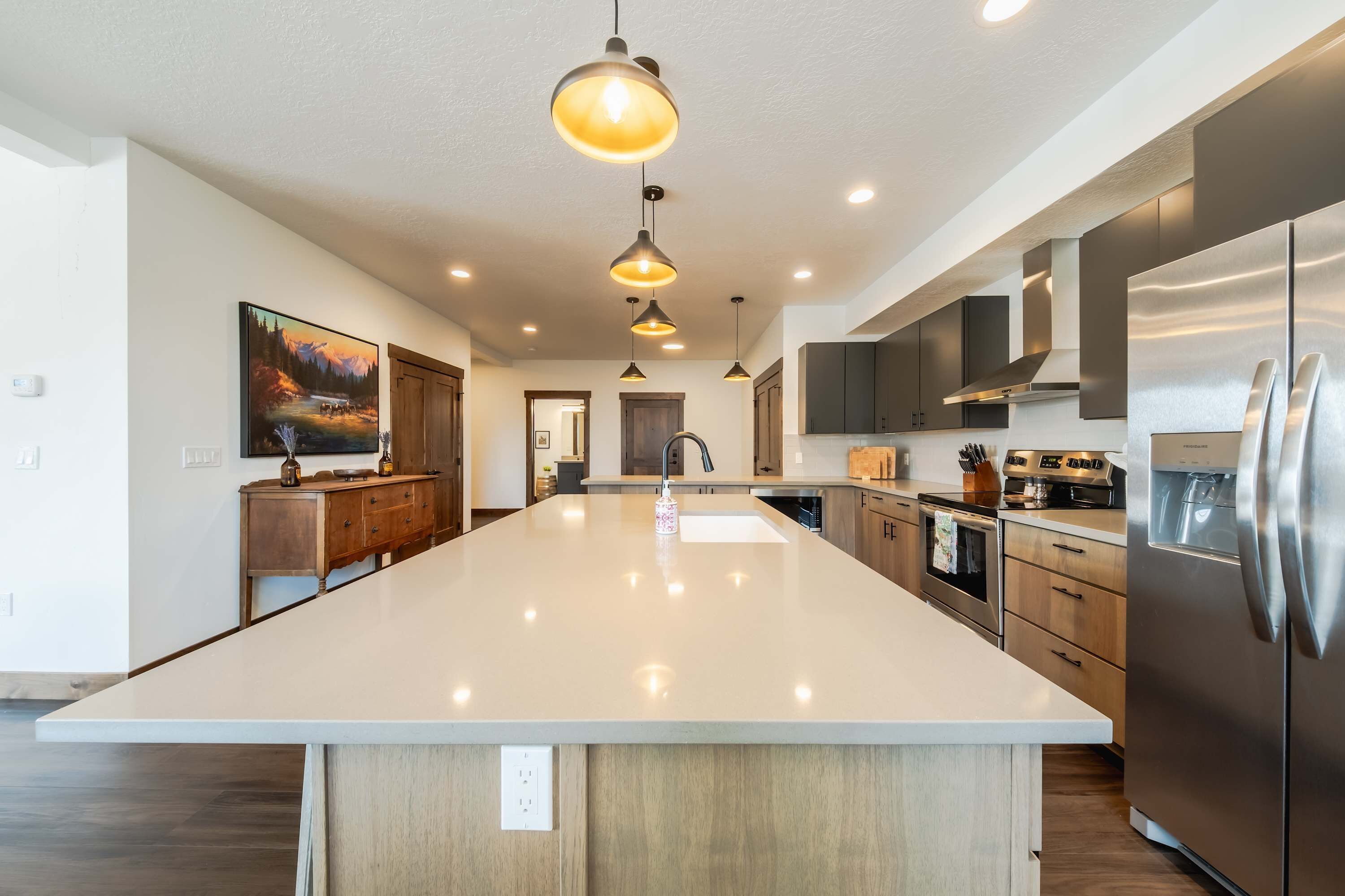 A spacious kitchen with a large island, stainless steel appliances, pendant lighting, and a painting on the wall.