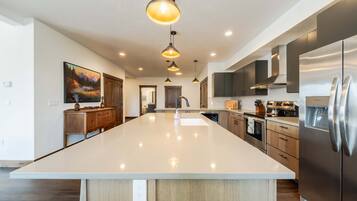 A spacious kitchen with a large island, stainless steel appliances, pendant lighting, and a painting on the wall.