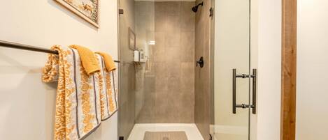 Un área de ducha con puerta de vidrio, un perchero con toallas estampadas y un cuadro en la pared.
