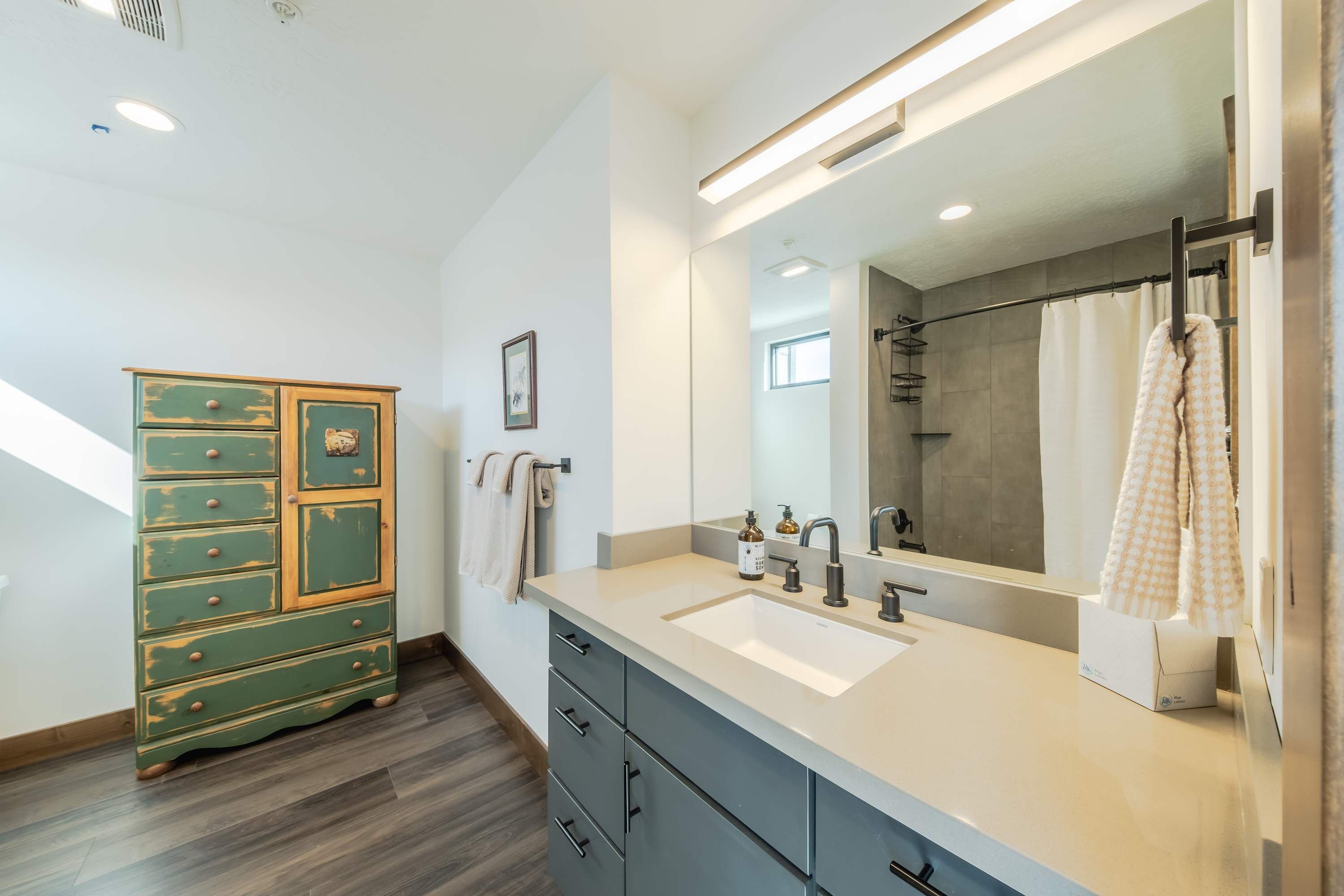 A modern bathroom with a large mirror, a sink, and a green dresser.