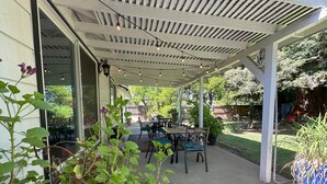 Un patio exterior con un área de estar cubierta, mesas y sillas.