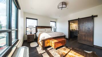 Un dormitorio moderno con una cama grande, un banco de madera, un ventanal amplio y una puerta corrediza.