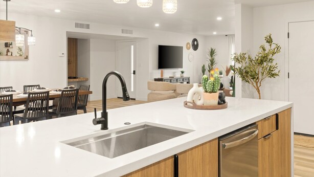 A modern kitchen with a large island, stainless steel appliances, pendant lighting, and a dining area with wooden chairs. - Ultimate Getaway, Pool, Hot Tub & Mini Golf (Tempe)