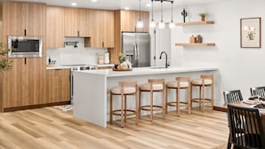 A modern kitchen with wooden cabinets, stainless steel appliances, a central island with bar stools, and pendant lighting. - Ultimate Getaway, Pool, Hot Tub & Mini Golf (Tempe)