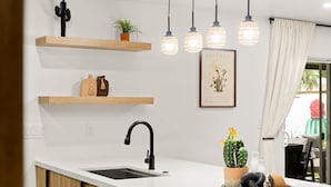 A modern kitchen with white countertops, black faucet, wooden shelves, hanging lights, and a cactus plant. - Ultimate Getaway, Pool, Hot Tub & Mini Golf (Tempe)