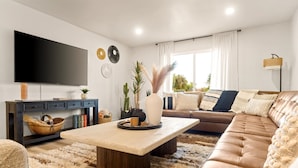 A modern living room with a flat-screen TV, a sofa, a coffee table, and decorative items. - Ultimate Getaway, Pool, Hot Tub & Mini Golf (Tempe)
