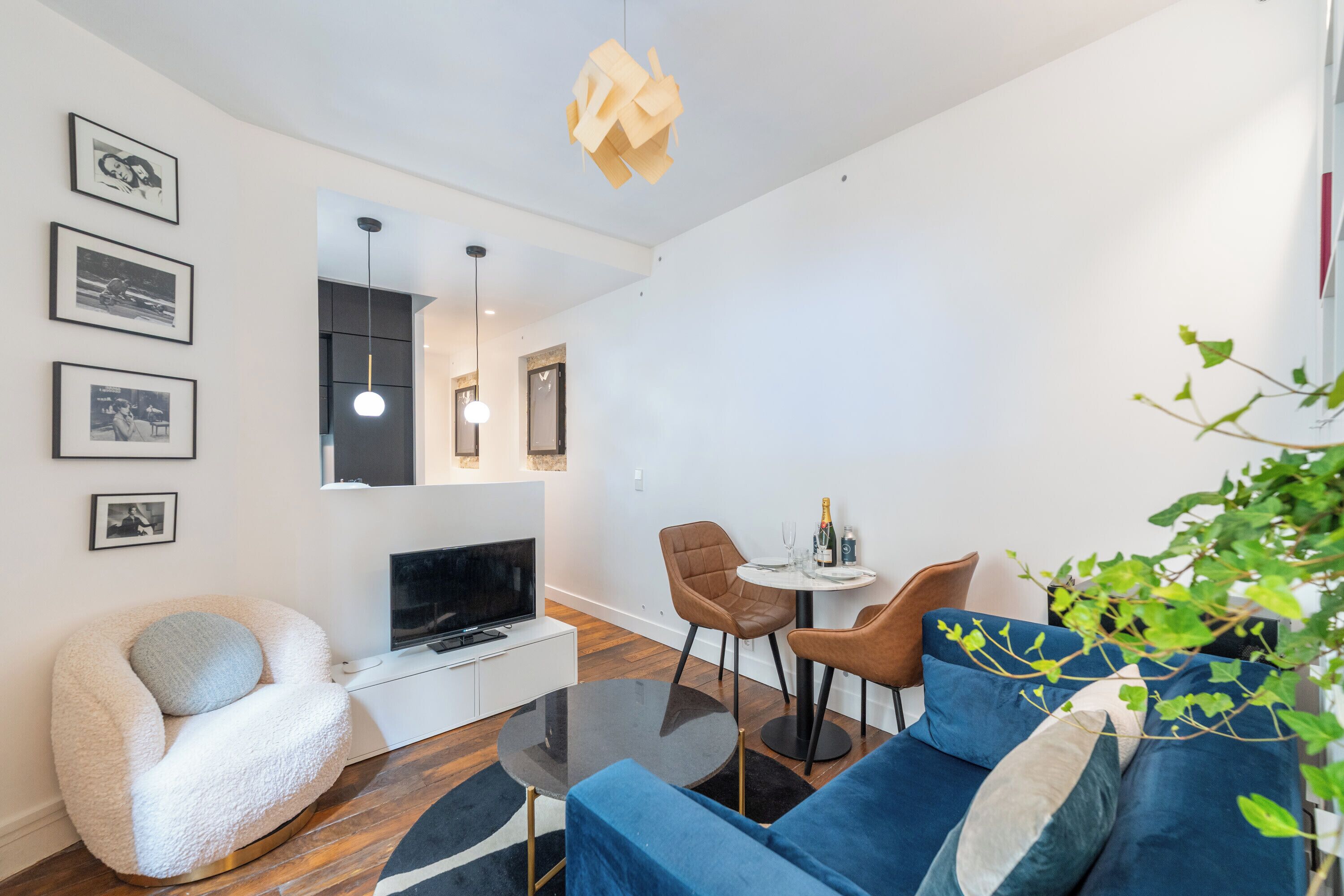 A modern living room with a sofa, a TV, a dining table with chairs, and framed pictures on the wall.